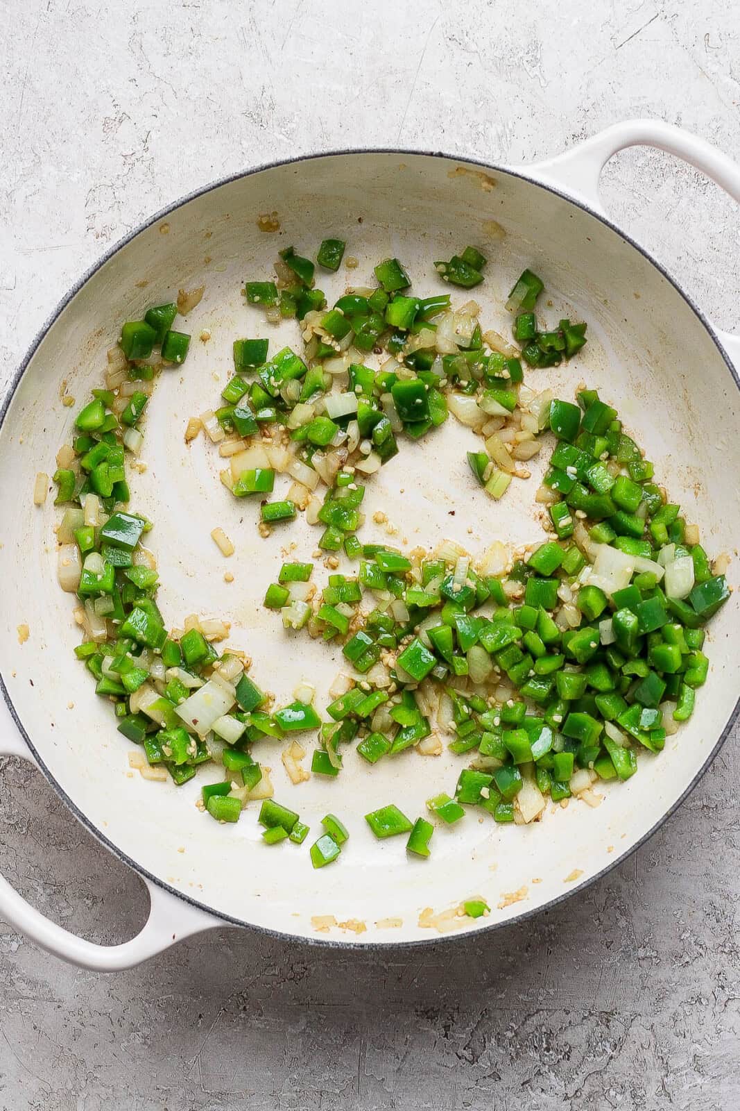 Onion, bell peppers, and garlic sautéing in a white braising pan.
