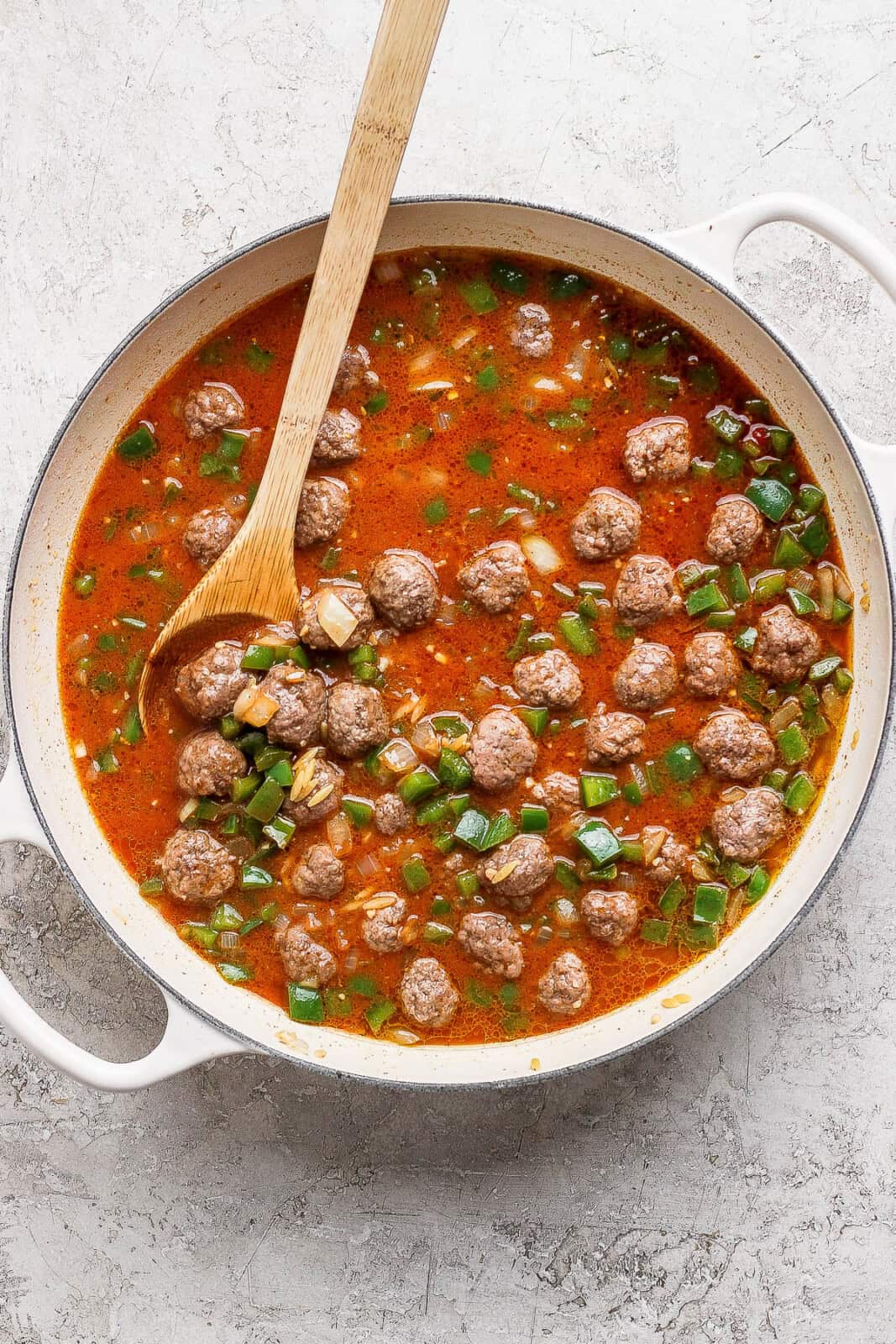 Sloppy joe orzo in a braising pan with a wooden spoon before the orzo is fully cooked.