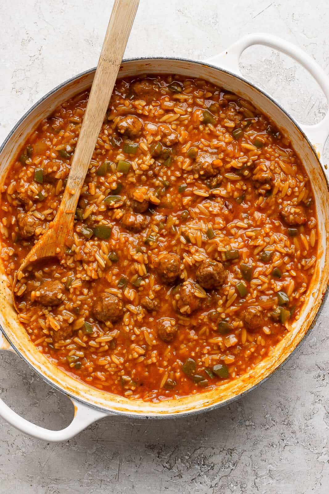 Sloppy joe orzo in a braising pan after the orzo is fully cooked with a wooden spoon sticking out the side.