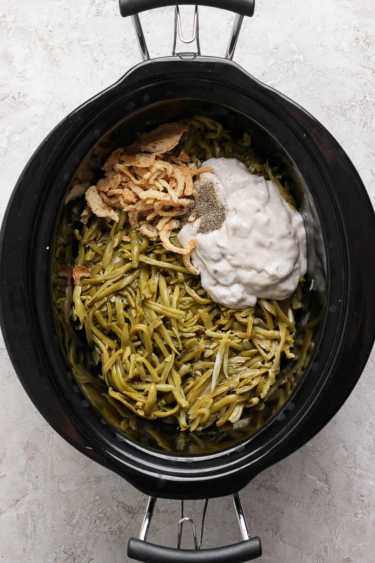 Ingredients for crock pot green bean casserole in a slow cooker before being mixed.