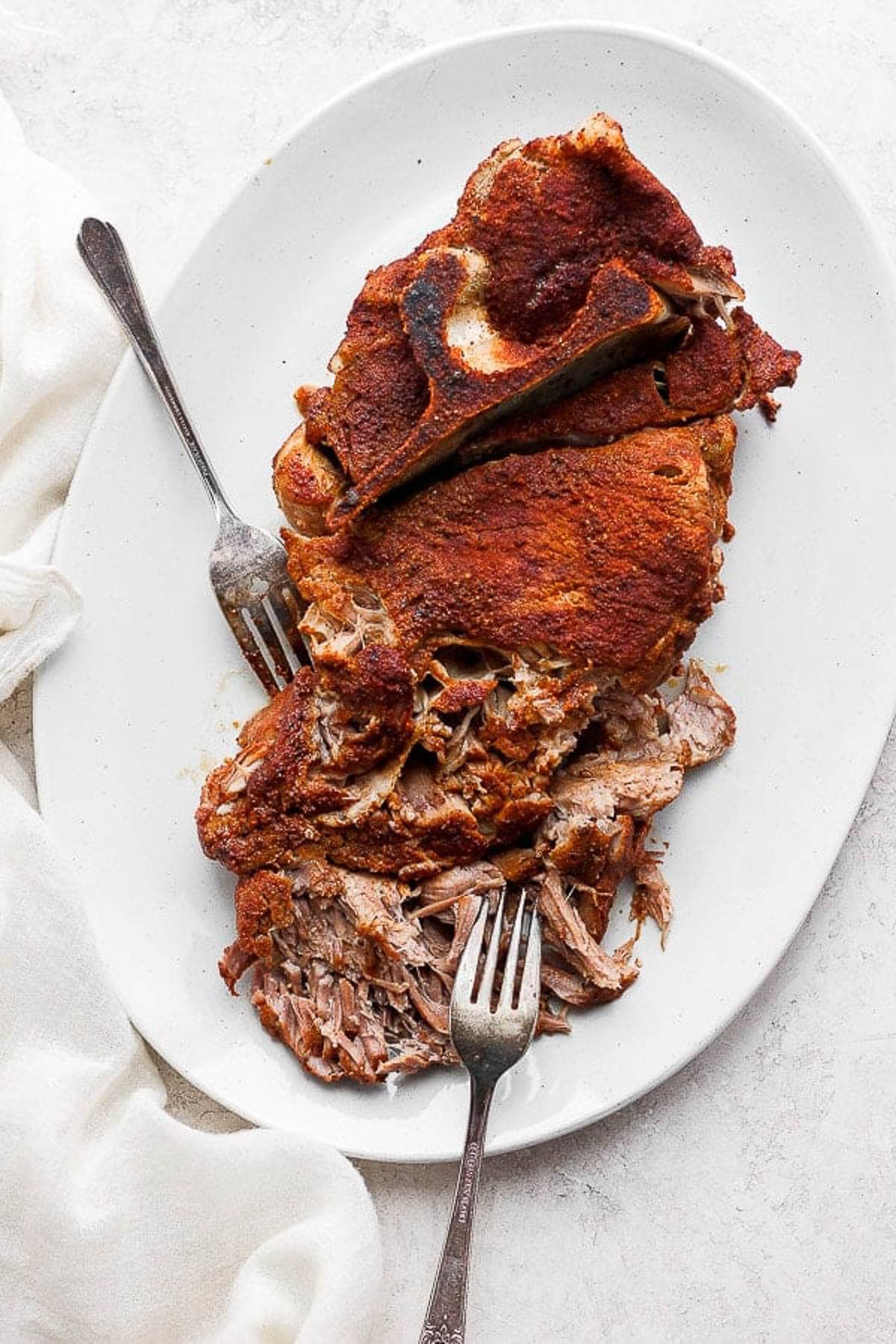 A slow cooker pulled pork shoulder on a platter after cooking and being shredded with two forks.