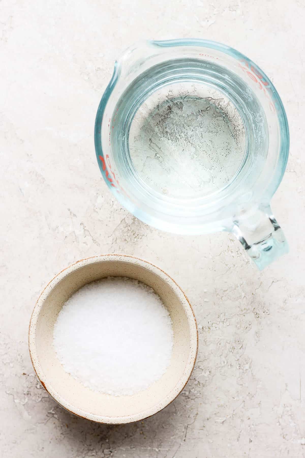 A bowl of kosher salt next to a glass measuring cup of water.