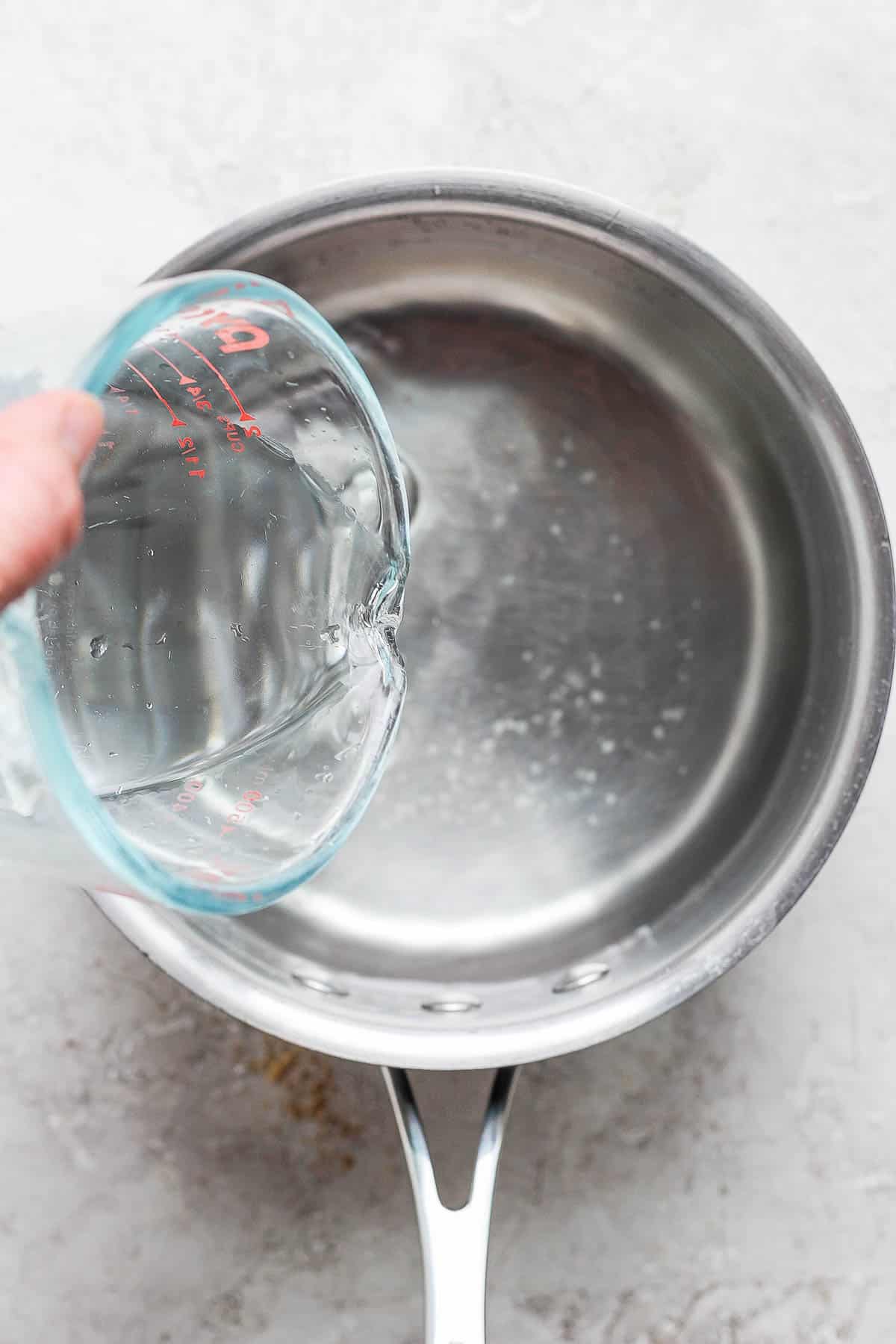 Water being poured from a glass measuring cup into a saucepan.