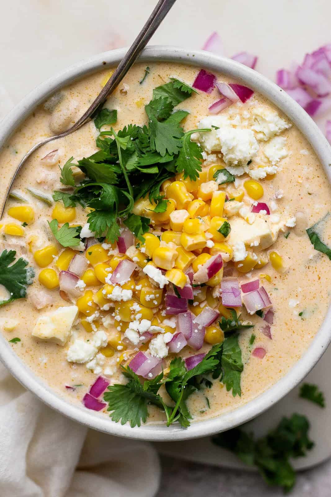 A fully topped bowl of Mexican street corn white chicken chili with a spoon sticking out the side.