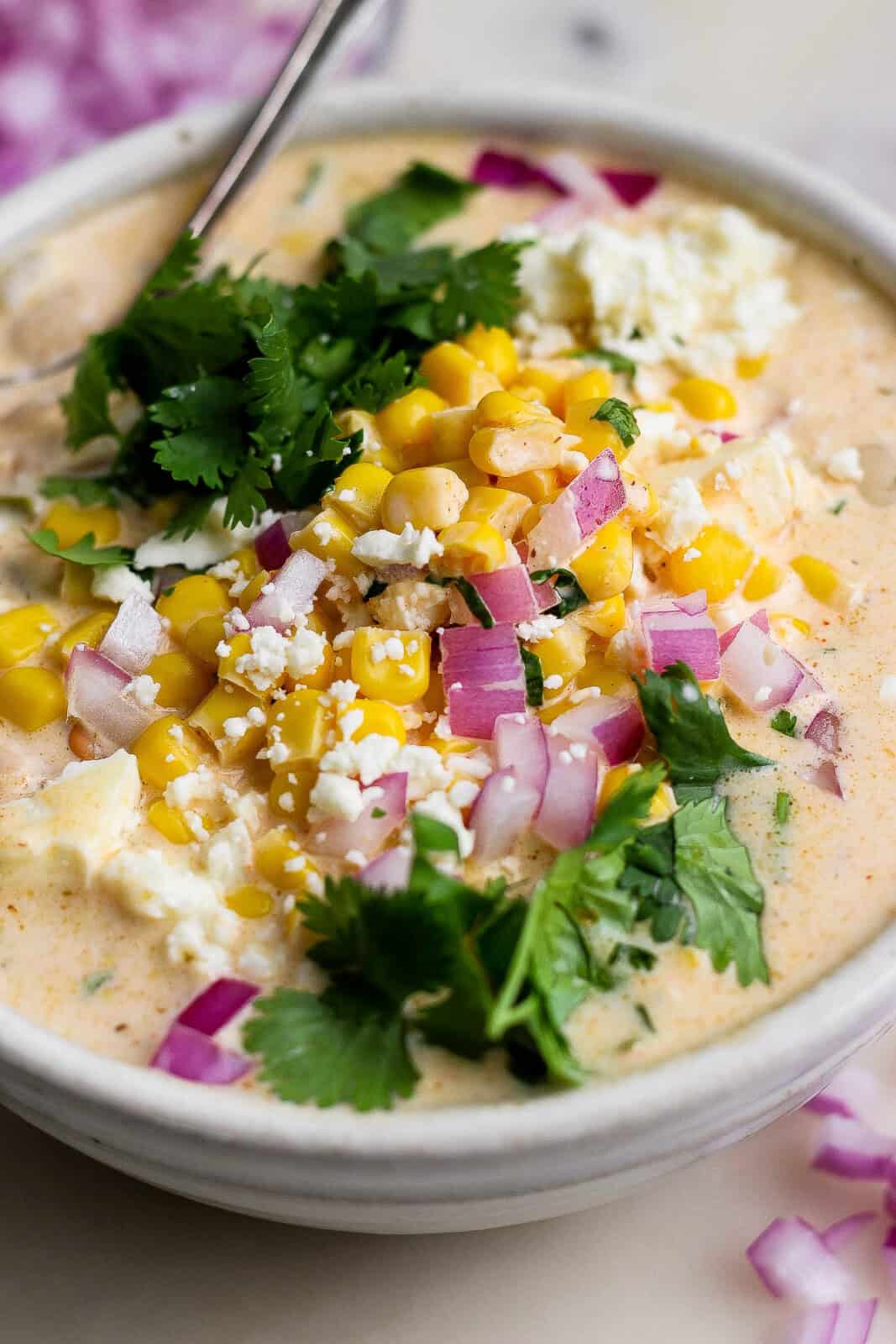 A bowl of Mexican street corn white chicken chili topped with street corn, fresh cilantro, red onions, and cotija cheese.