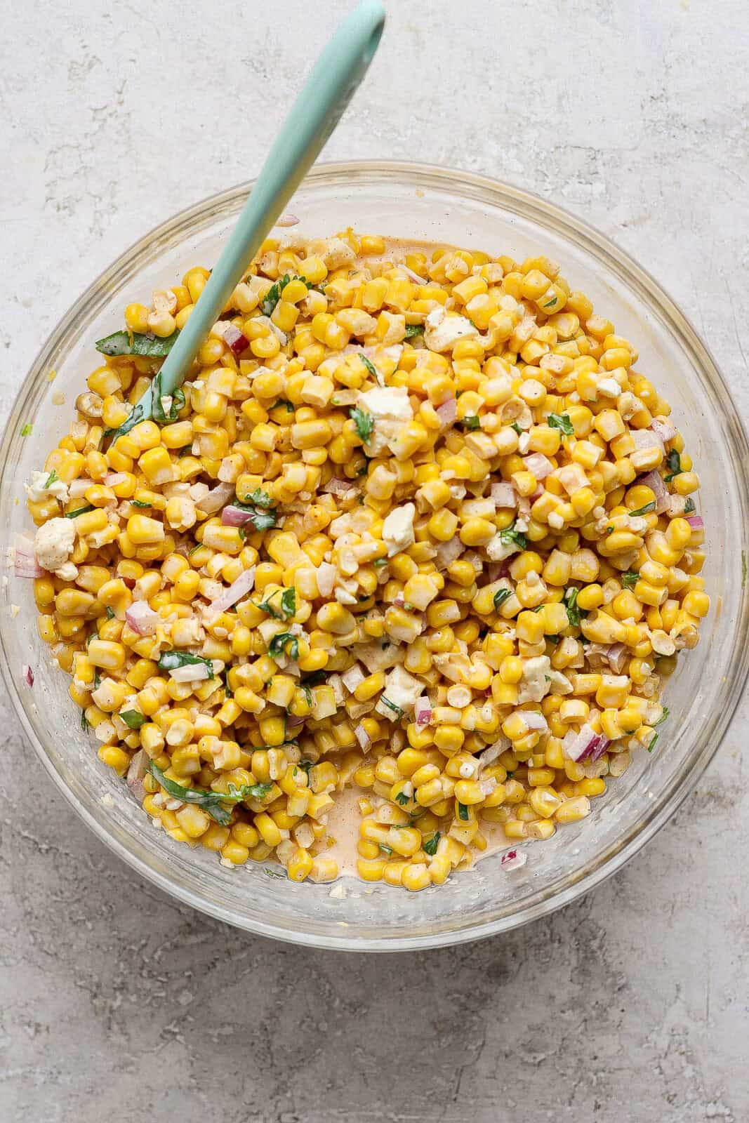 A large glass bowl of Mexican street corn with a rubber spatula in it.