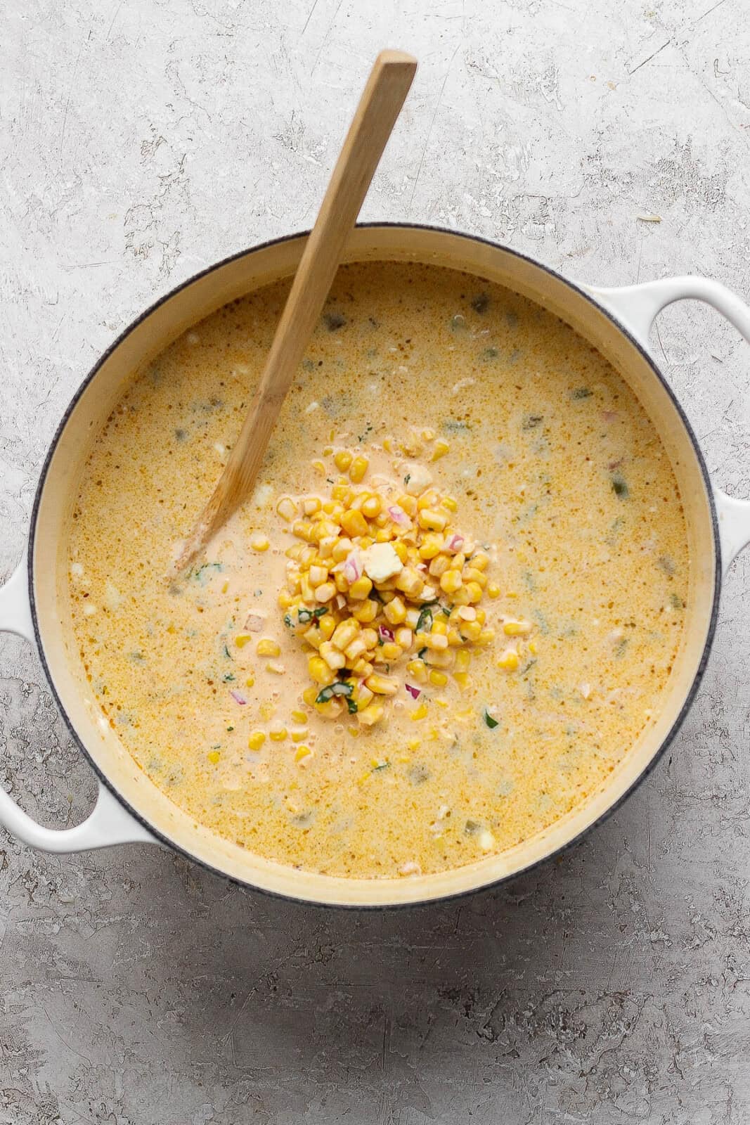 A pot of Mexican street corn white chicken chili with a wooden spoon sticking out the side and the street corn mixture added to the pot.