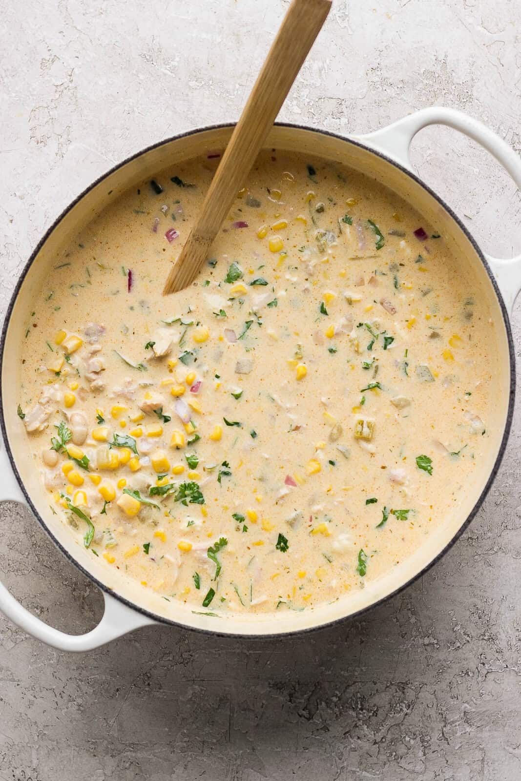 A fully mixed pot of Mexican street corn white chicken chili with a wooden spoon sticking out the side.