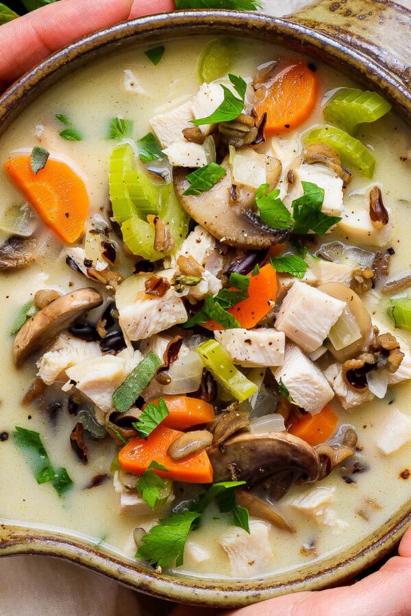 Two hands holding a bowl of turkey wild rice soup.