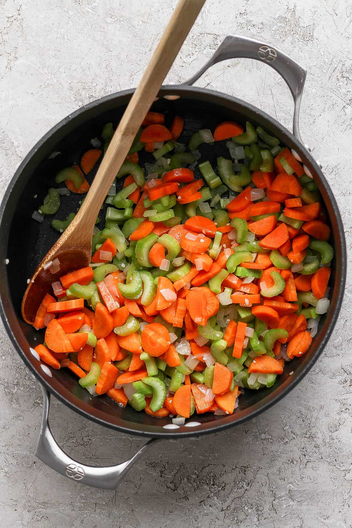 Onion, garlic, carrots and celery sautéing in a soup pot with a wooden spoon sticking out the side.