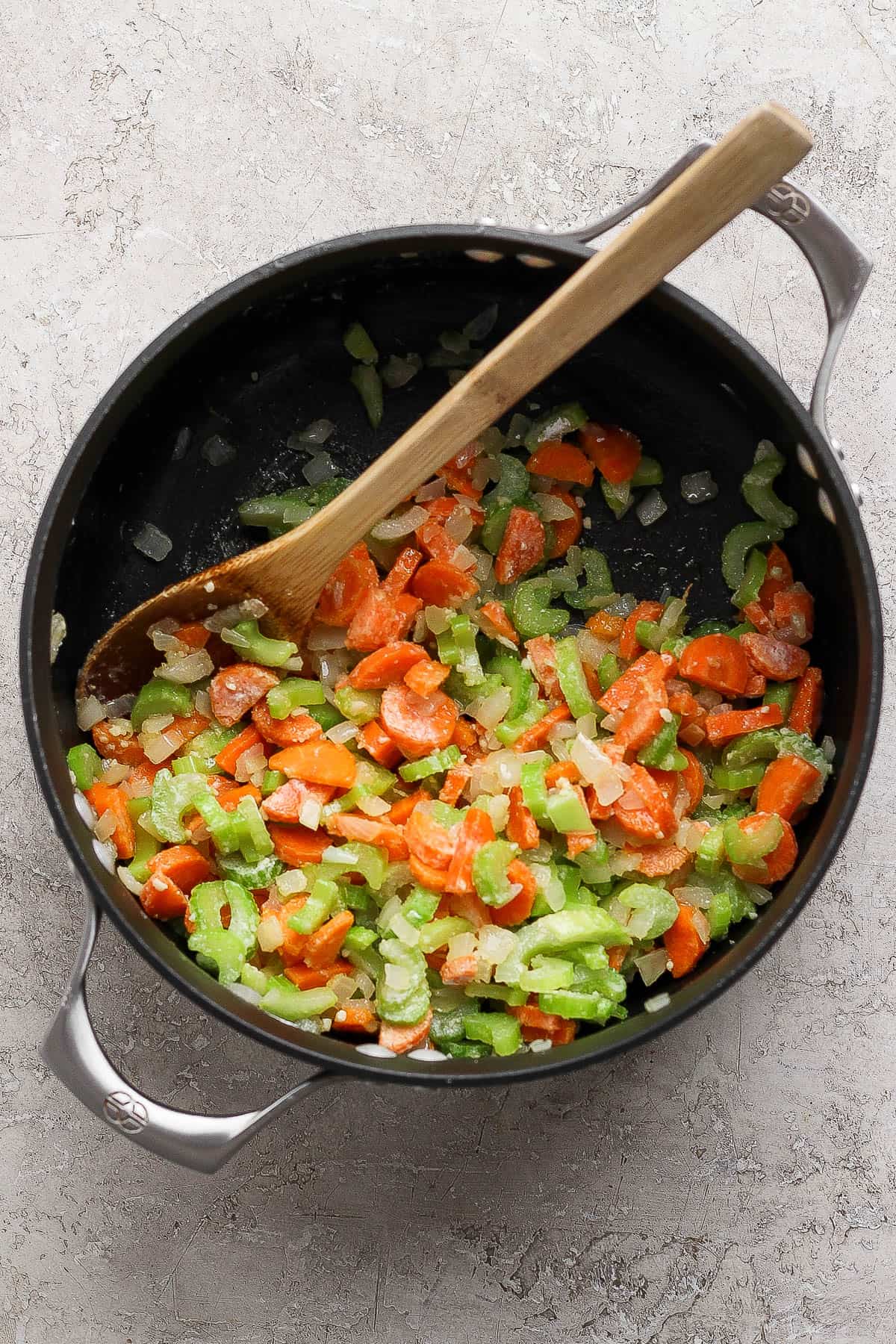 Sautéed vegetables in a soup pot coated in arrowroot powder with a wooden spoon.
