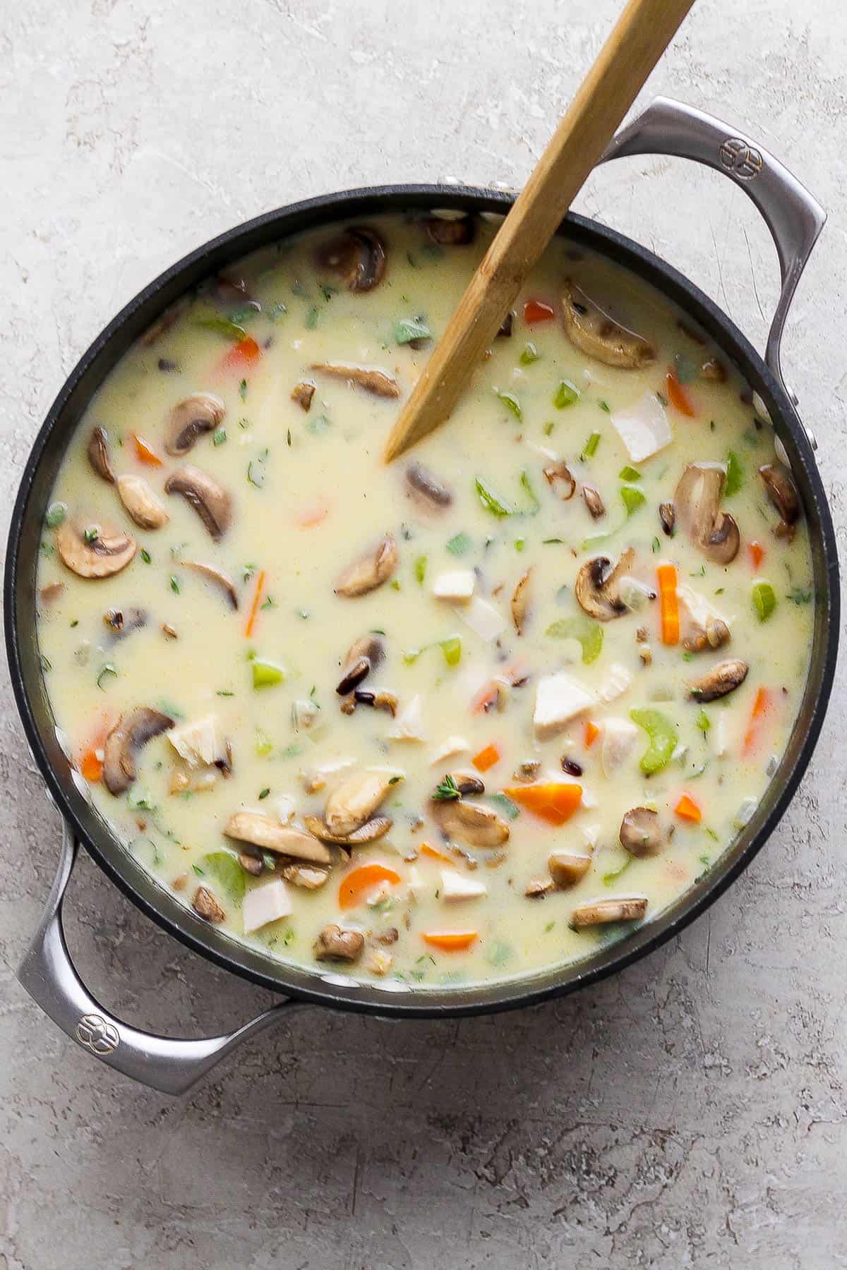 A soup pot of turkey wild rice soup with a wooden spoon sticking out the side.