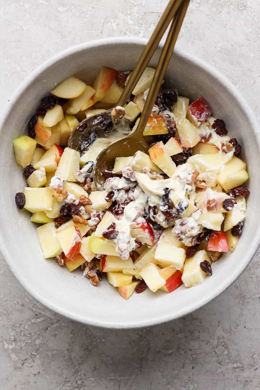 Apples, walnuts, raisins, and mayo mixed in a bowl to make apple and walnut salad.