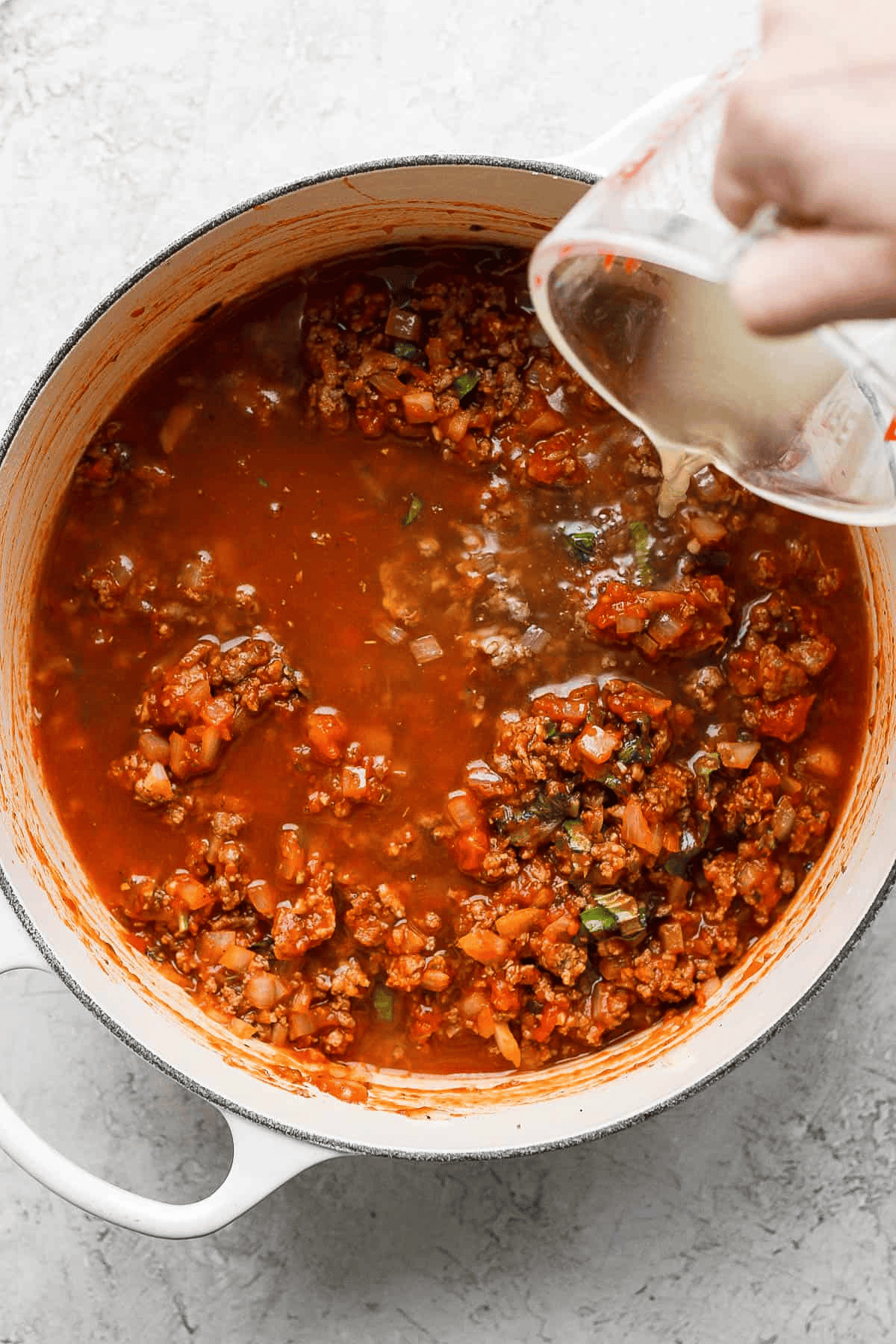Chicken broth being poured into a pot of lasagna soup.