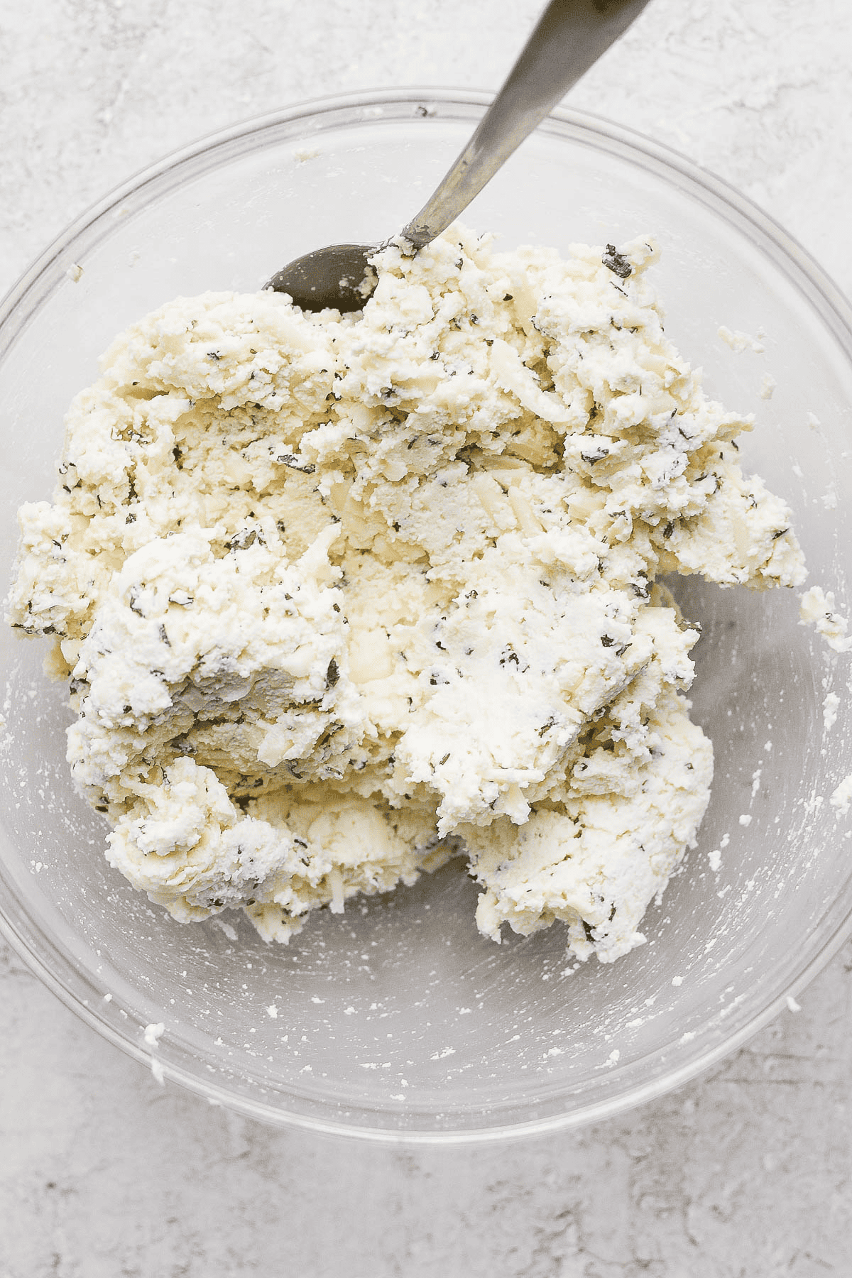 The ricotta mixture for lasagna soup fully mixed in a glass bowl with a spoon sticking out the side.