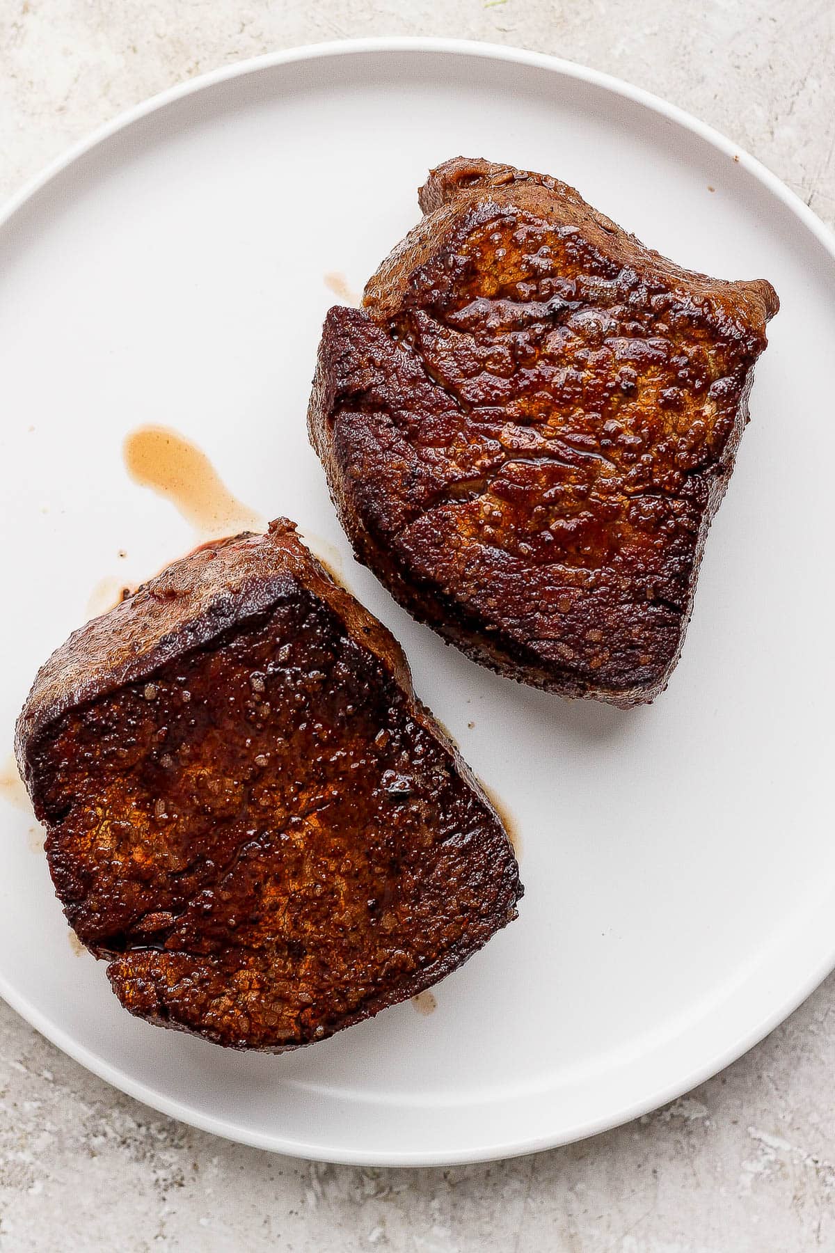 Two cast iron skillet filet mignon steaks resting on a white plate.