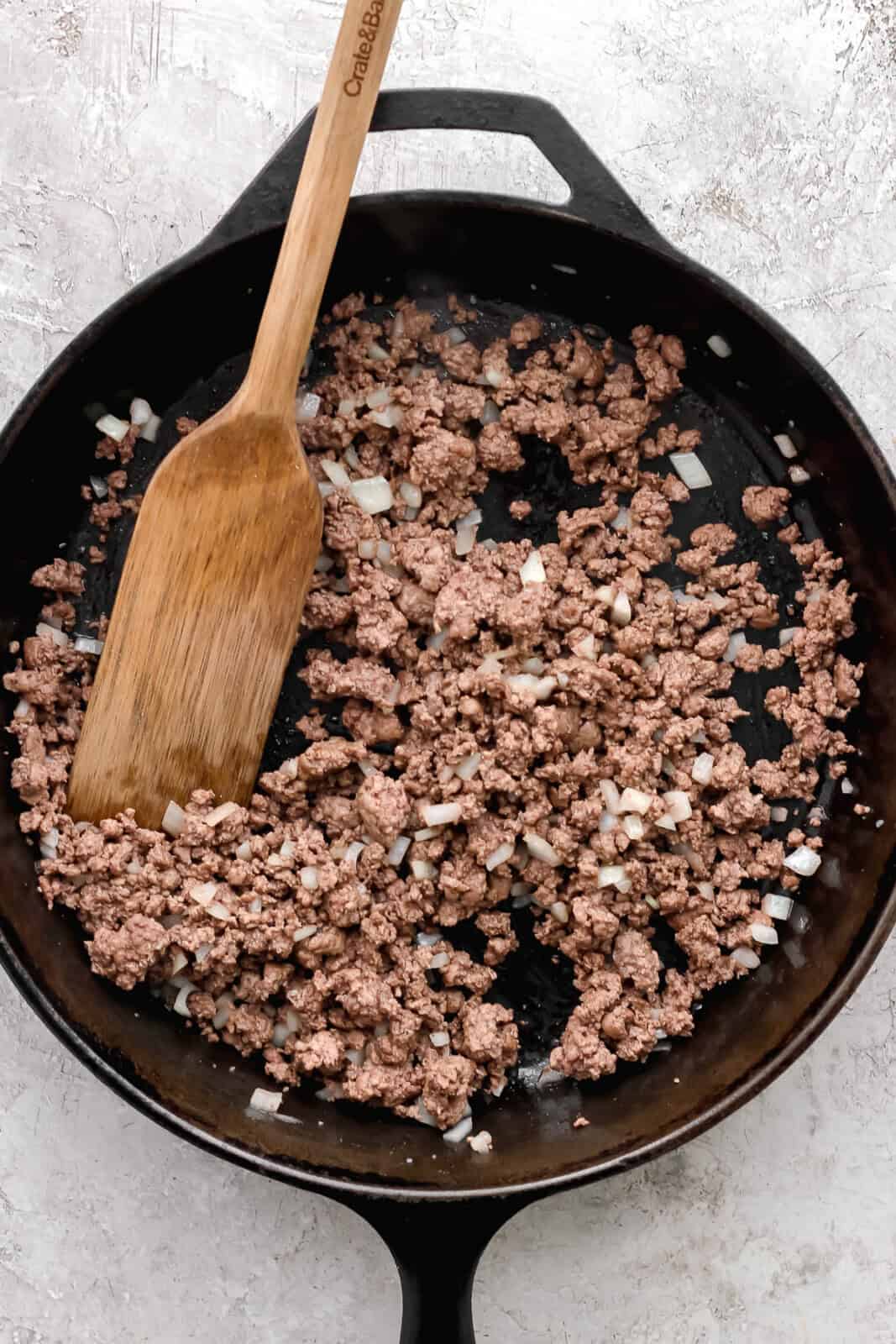 Onion mixed into ground beef in a cast iron skillet to make meat mixture for cheeseburger quesadillas.