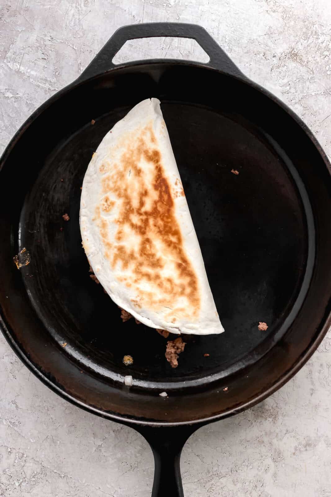 Cheeseburger quesadilla folded in half in a cast iron skillet.