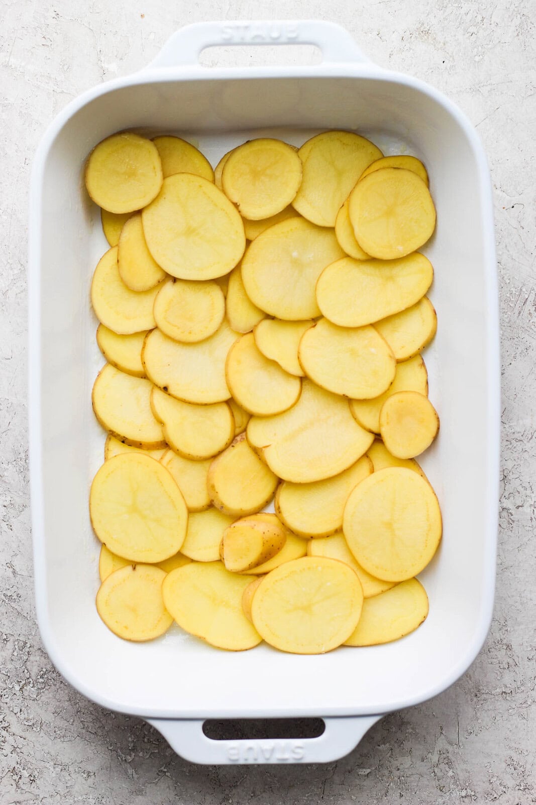 Sliced potatoes covering the bottom of a baking dish to make cheesy scalloped potatoes.