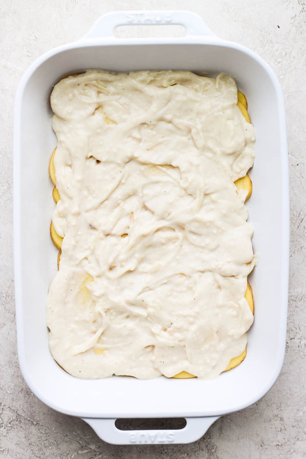 Cream sauce covering the sliced potatoes in a casserole dish to make cheesy scalloped potatoes.