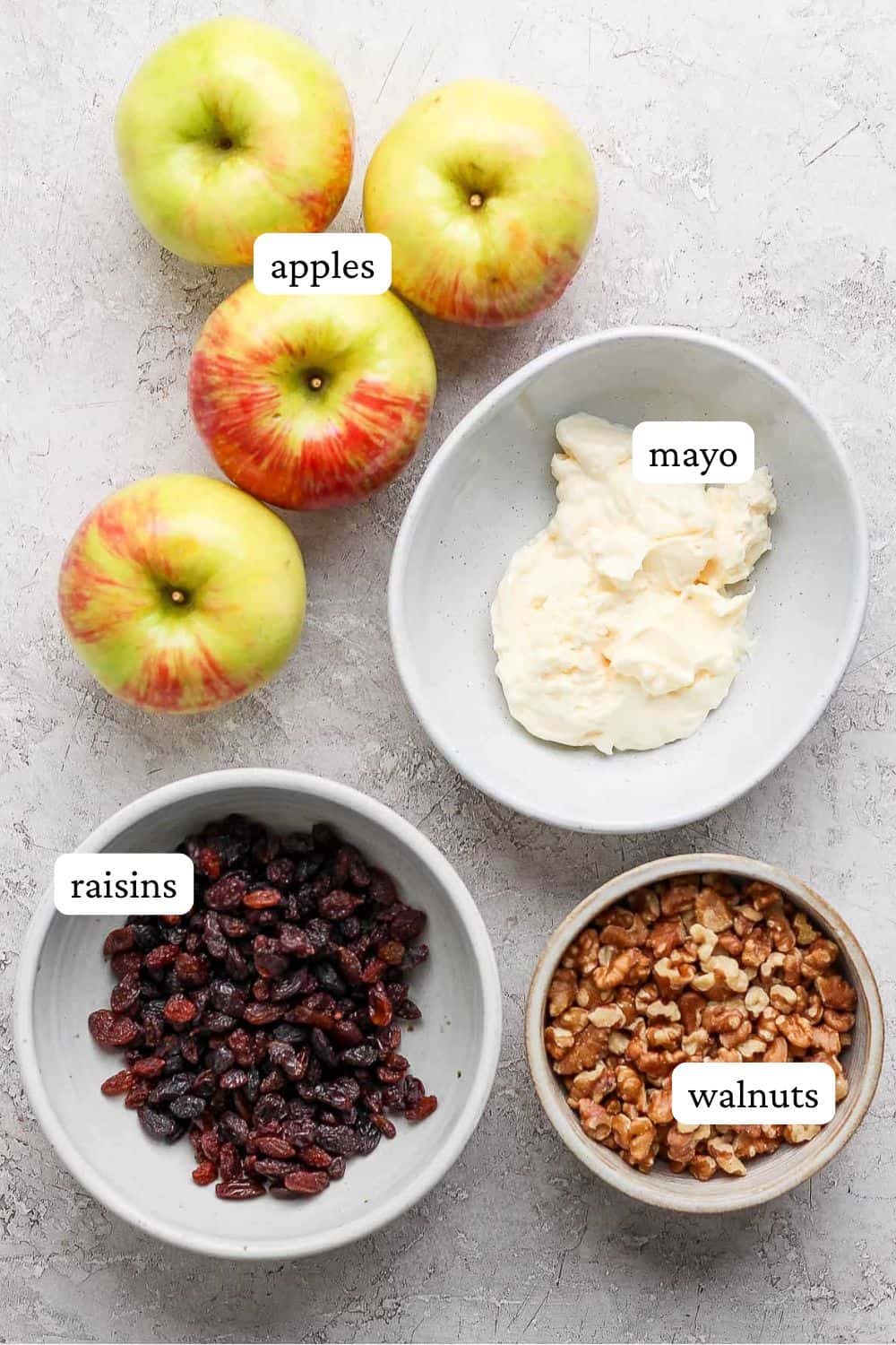 Ingredients for apple and walnut salad including 4 apples, a bowl of mayo, a bowl of raisins, and a bowl of walnuts.