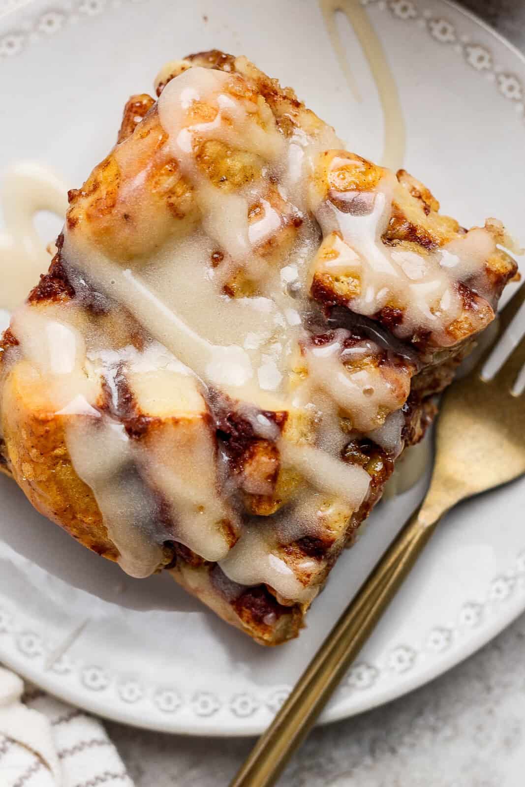 A square piece of cinnamon roll casserole on a plate with a fork.