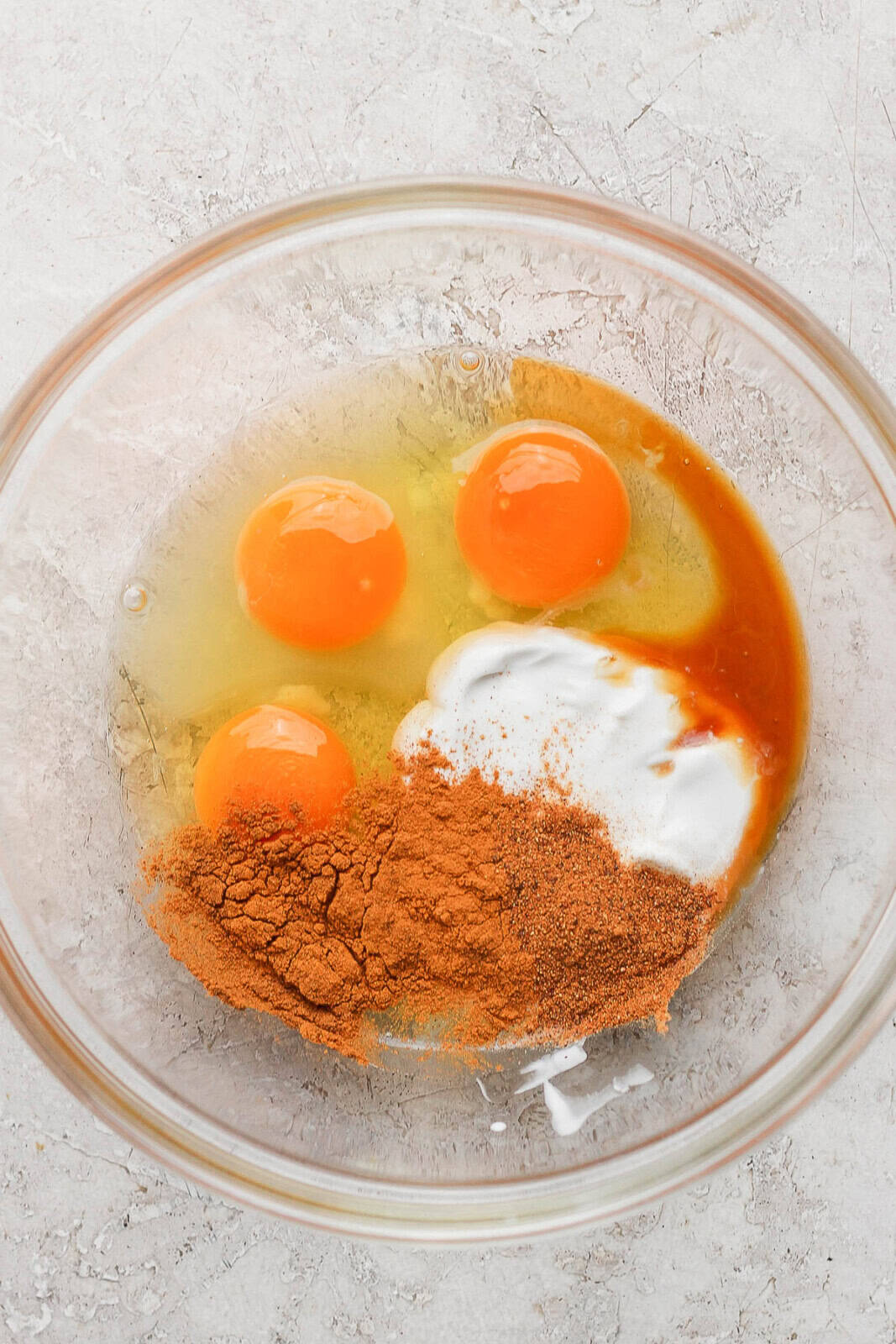 Eggs, vanilla, cinnamon, nutmeg, and creamer in a bowl unmixed to make the binder for cinnamon roll casserole.
