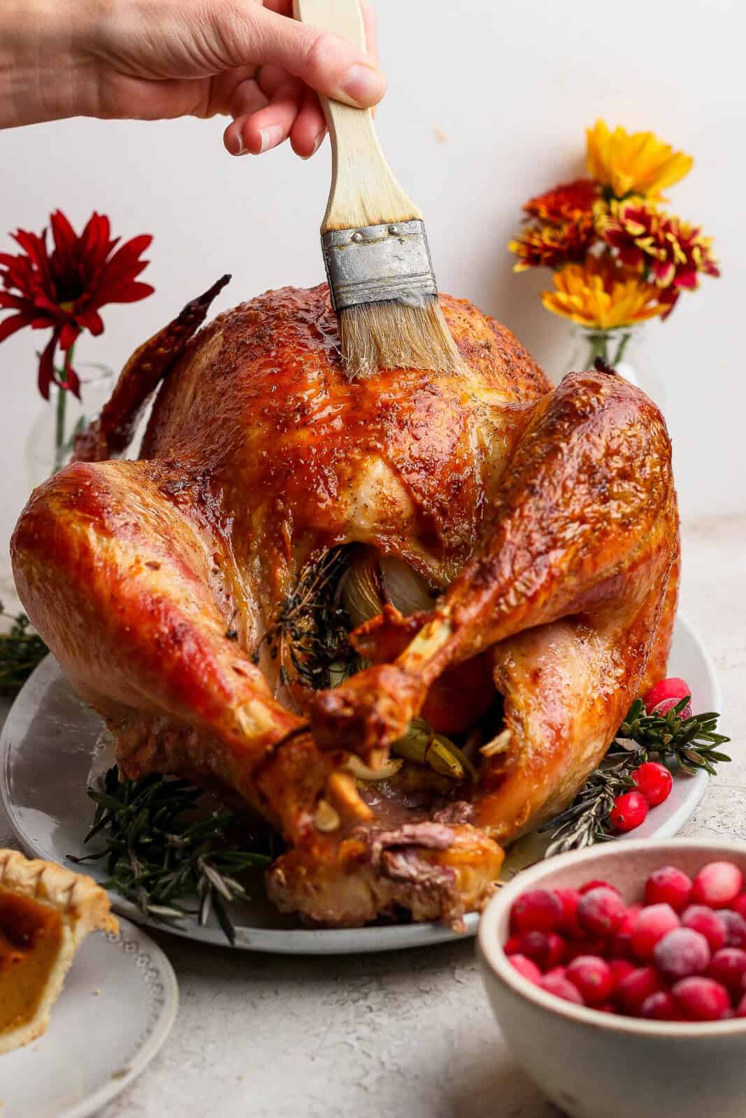 A cooked whole grilled turkey on a platter with someone basting it with a brush.