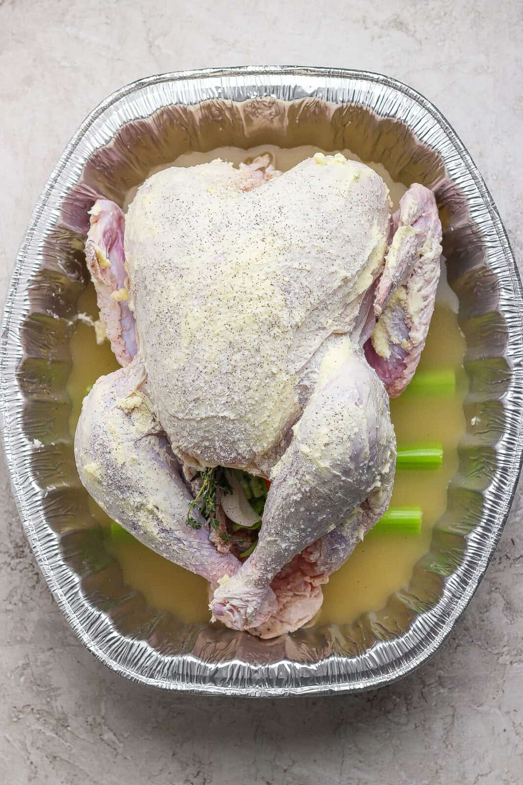 A prepared whole turkey with butter and salt inside the roasting pan ready for the grill.