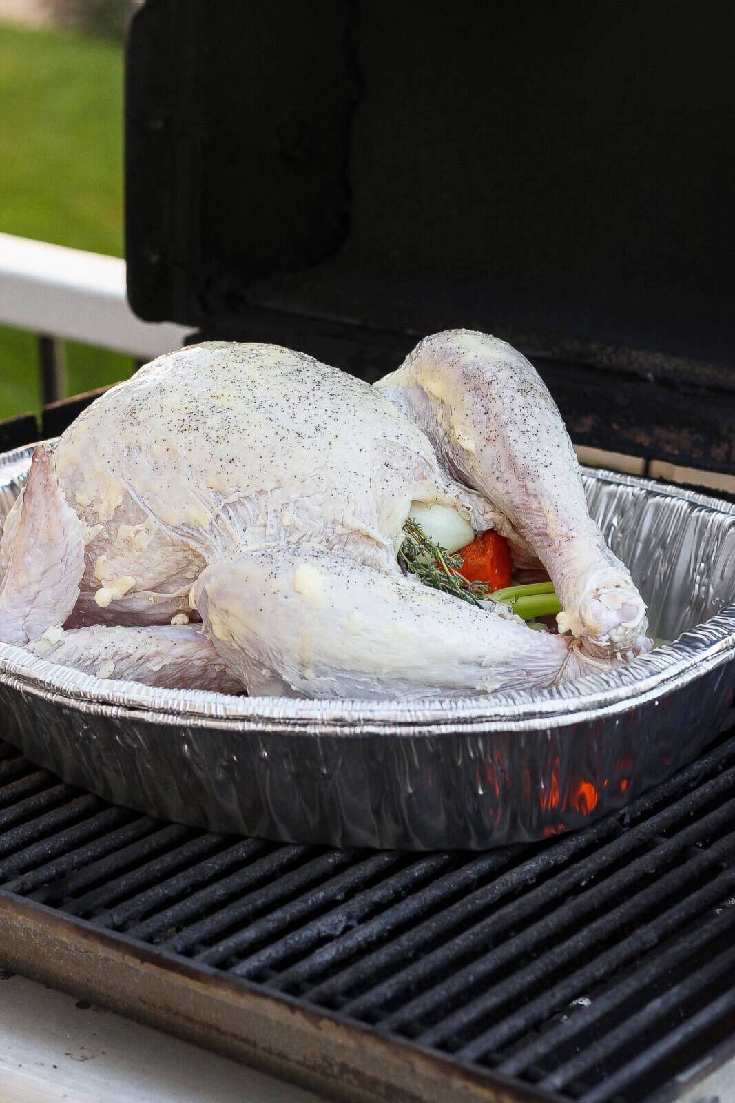 A turkey in an aluminum roasting pan that just got set on the grill and is still raw.