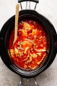 Lasagna soup in a slow cooker with a wooden spoon sticking out the side.