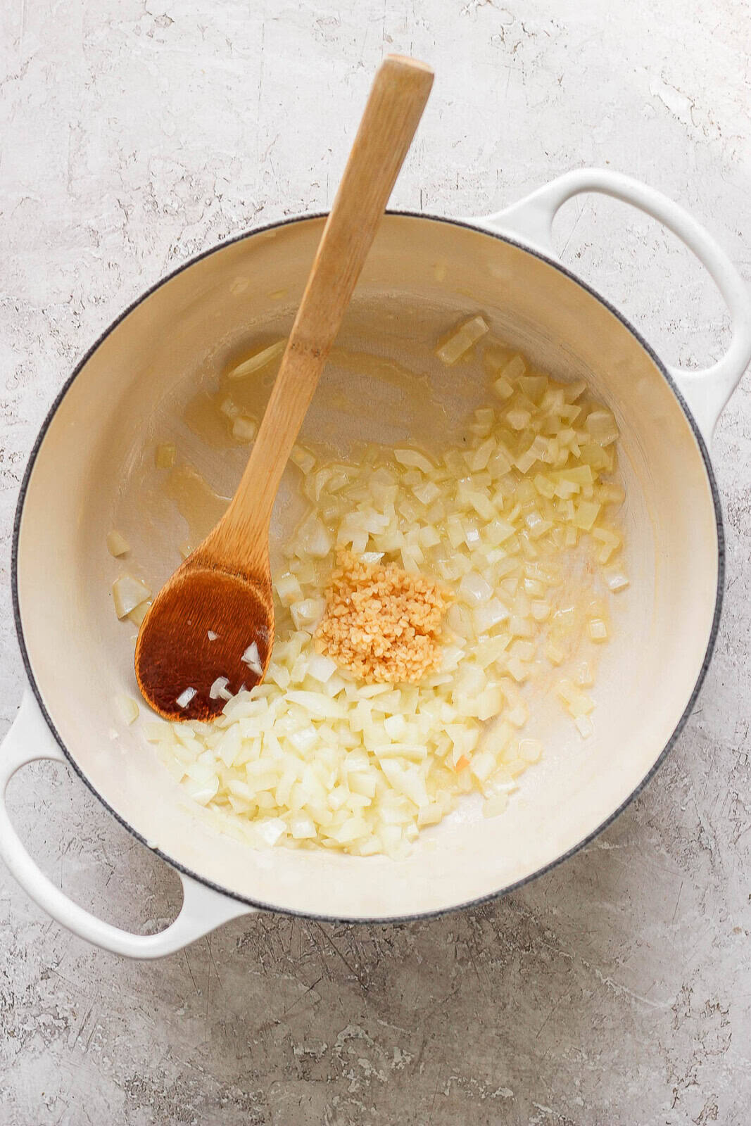 Chopped onion and minced garlic in a dutch oven with a wooden spoon.
