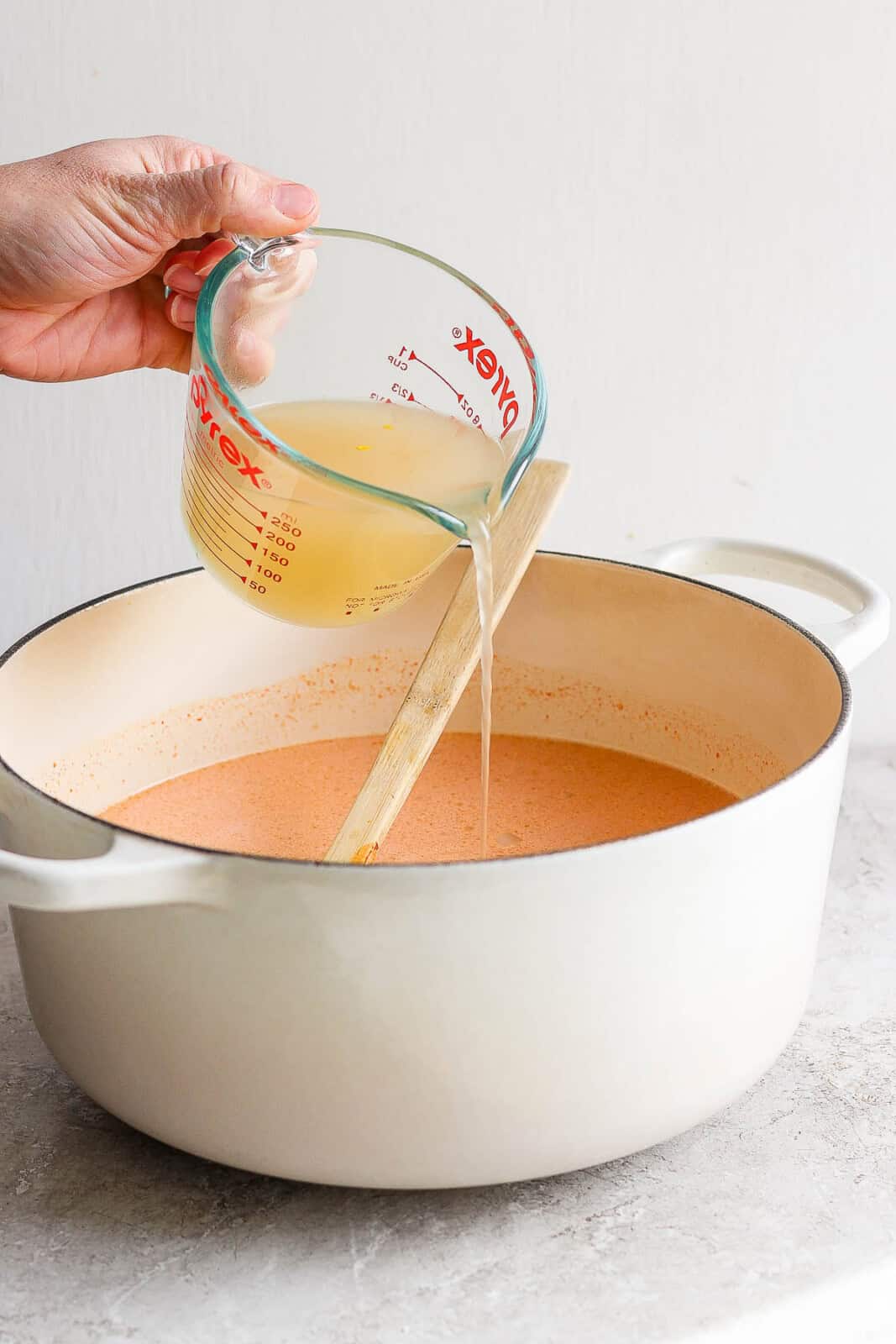 A hand pouring broth into a dutch oven to make the curry ramen broth.