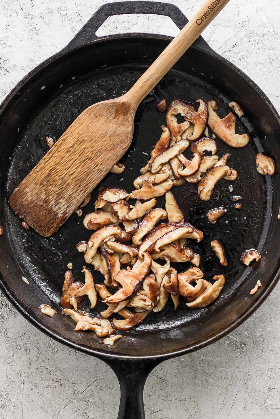 Sliced shiitake mushrooms cooking in a cast iron skillet.