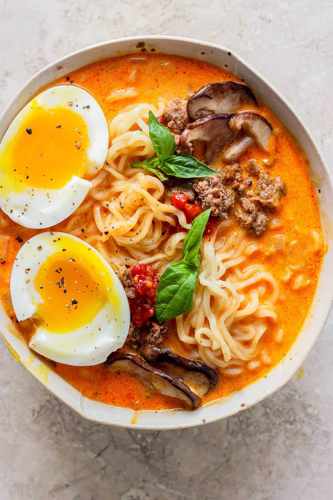 A bowl of curry ramen topped with a soft boiled egg and fresh basil.