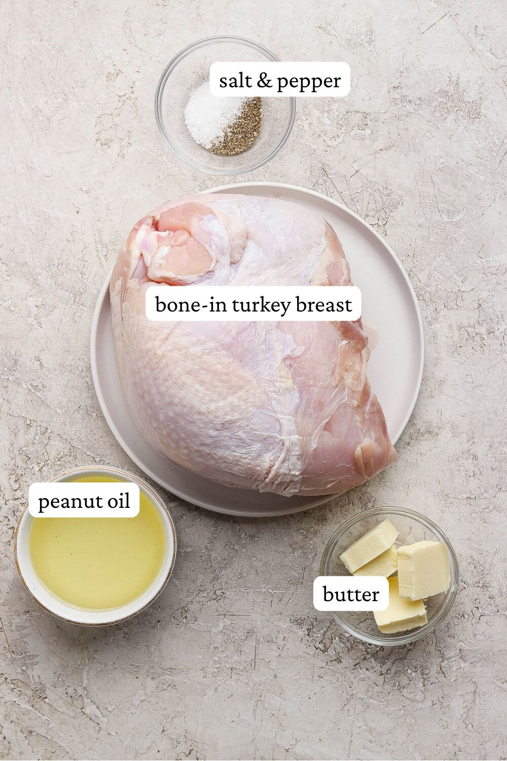 A thawed bone-in turkey breast on a plate next to bowls of peanut oil, butter, salt and pepper with labels.