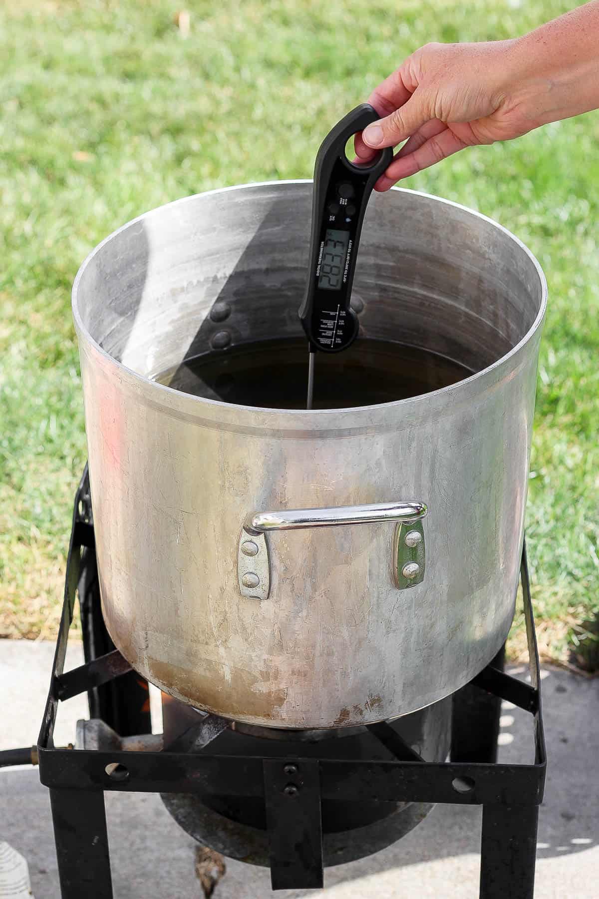 Peanut oil being heated in a large fryer and someone is checking the temperature of the oil.