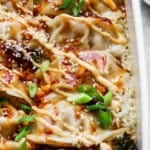 A casserole dish filled with a dumpling bake with rice, broccolini, dumplings (or potstickers), spicy mayo, sauce, green onions and sesame seeds.