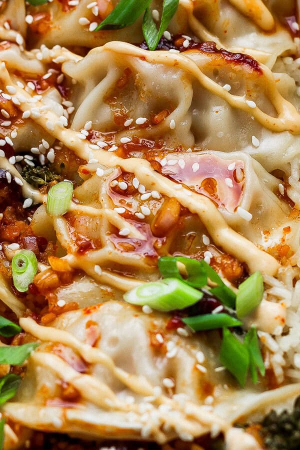 A casserole dish filled with a dumpling bake with rice, broccolini, dumplings (or potstickers), spicy mayo, sauce, green onions and sesame seeds.