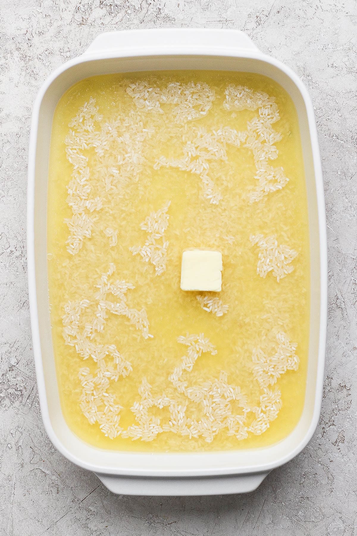 Rice, chicken stock, and butter in a casserole dish to make dumpling bake.