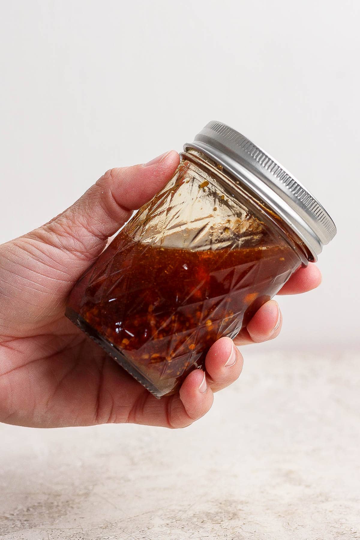 A hand holding a glass jar with a lid containing sauce to pour over the dumpling bake.