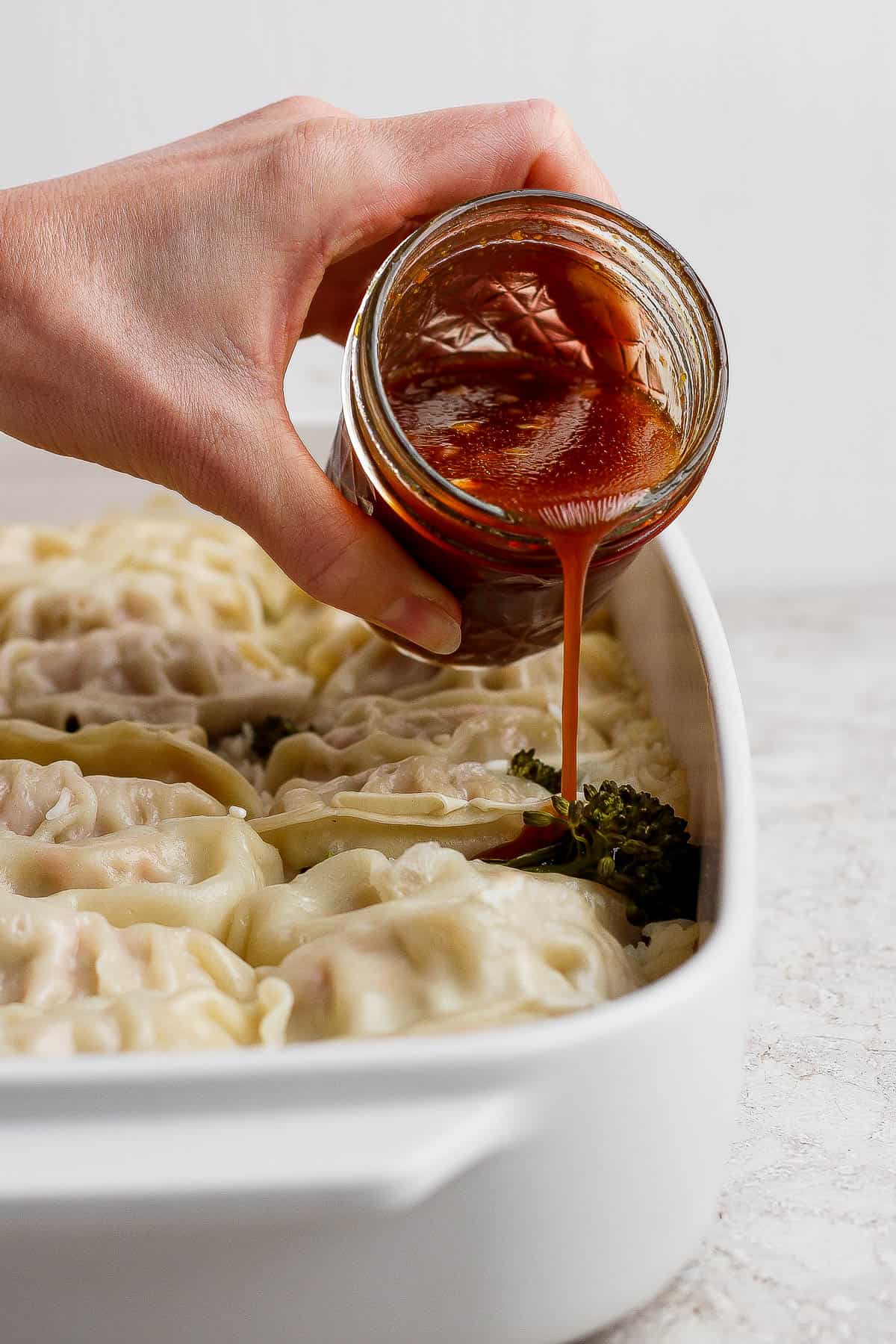 A hand pouring sauce over the baked dumpling bake.