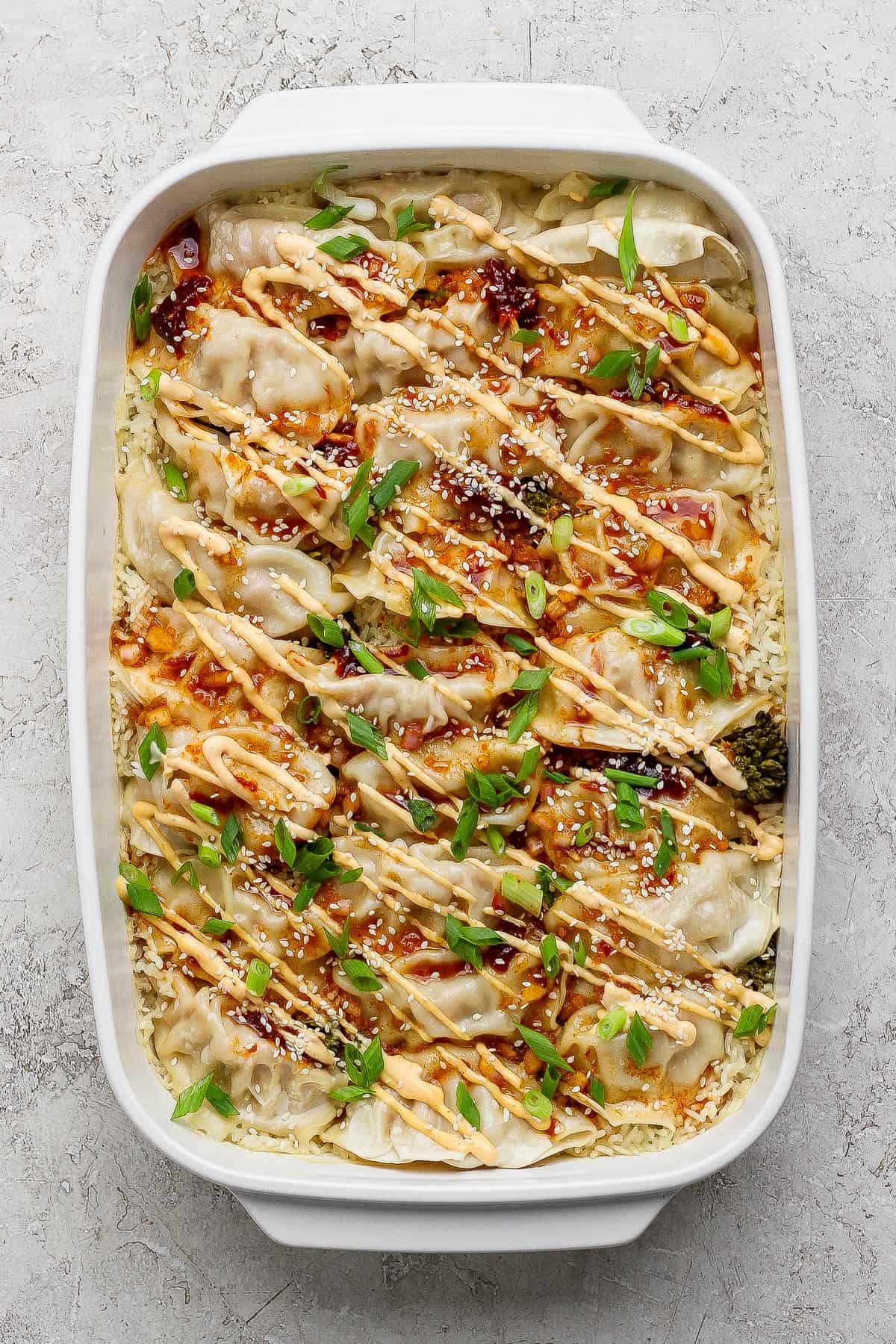 Dumpling bake topped with spicy mayo, sliced green onions, and sesame seeds.