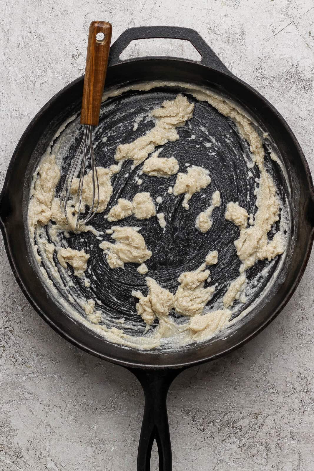 A whisk sticking out of a cast iron skillet and a butter and flour mixed together inside to create a roux.