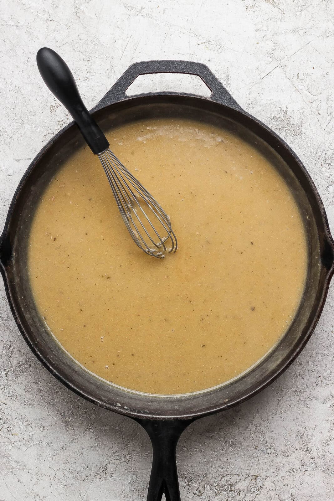 Dairy free and gluten free gravy in a cast iron skillet with a whisk sticking out. 