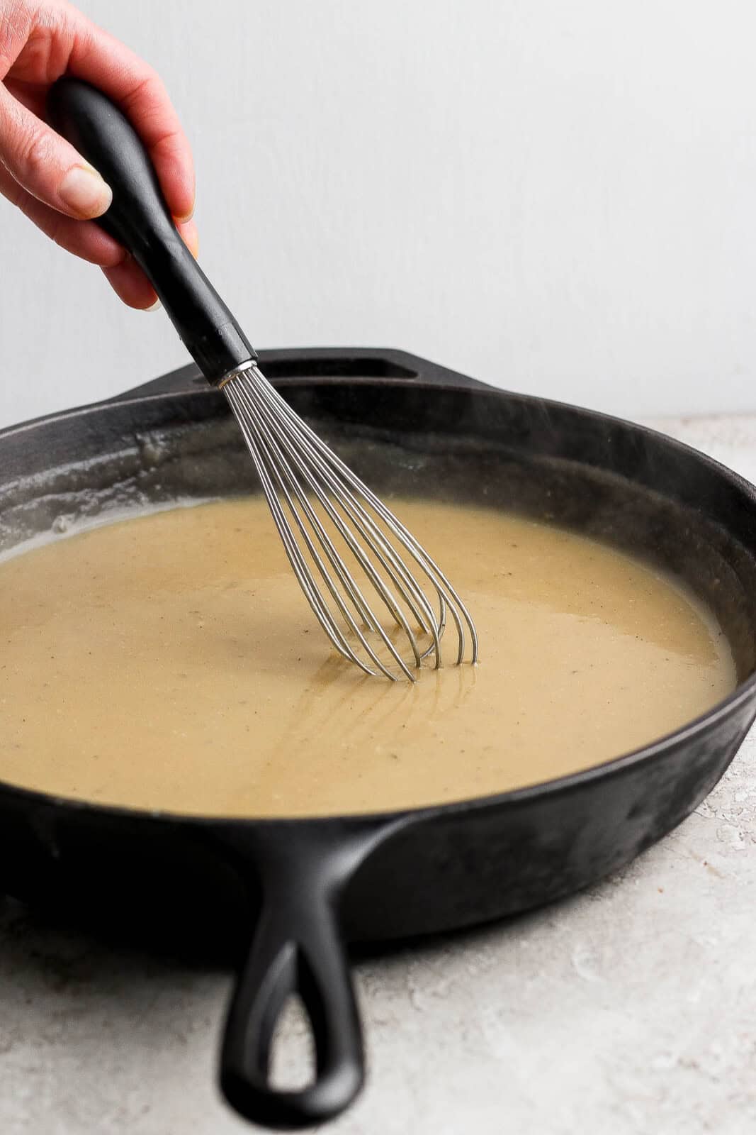 A cast iron skillet filled with gravy with someone whisking it.