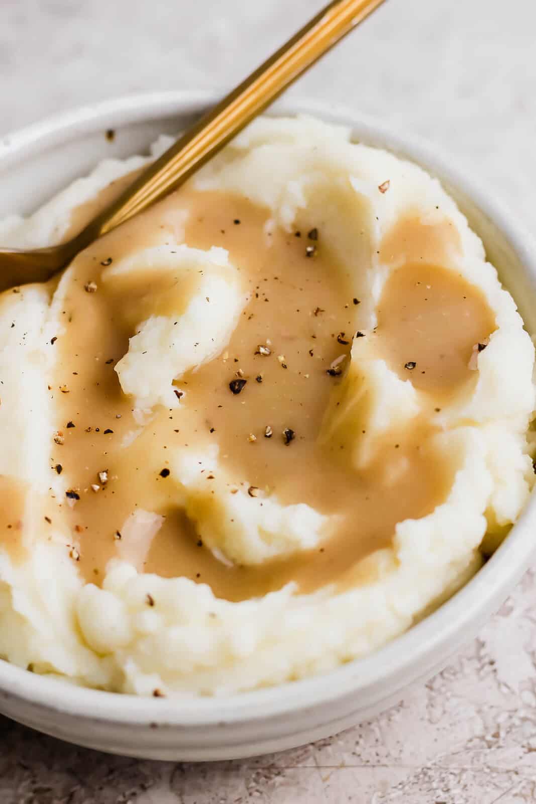 A bowl of mashed potatoes with gluten and dairy free gravy on top with fresh cracked pepper.