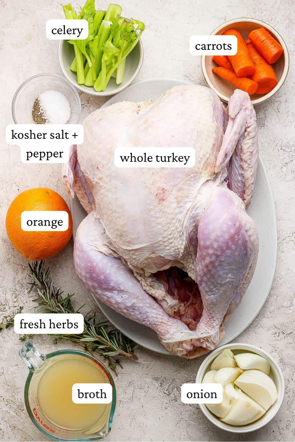 Ingredients for grilled turkey separated out so you can see the onion, broth, fresh herbs, orange, whole turkey, carrots, celery and salt and pepper.