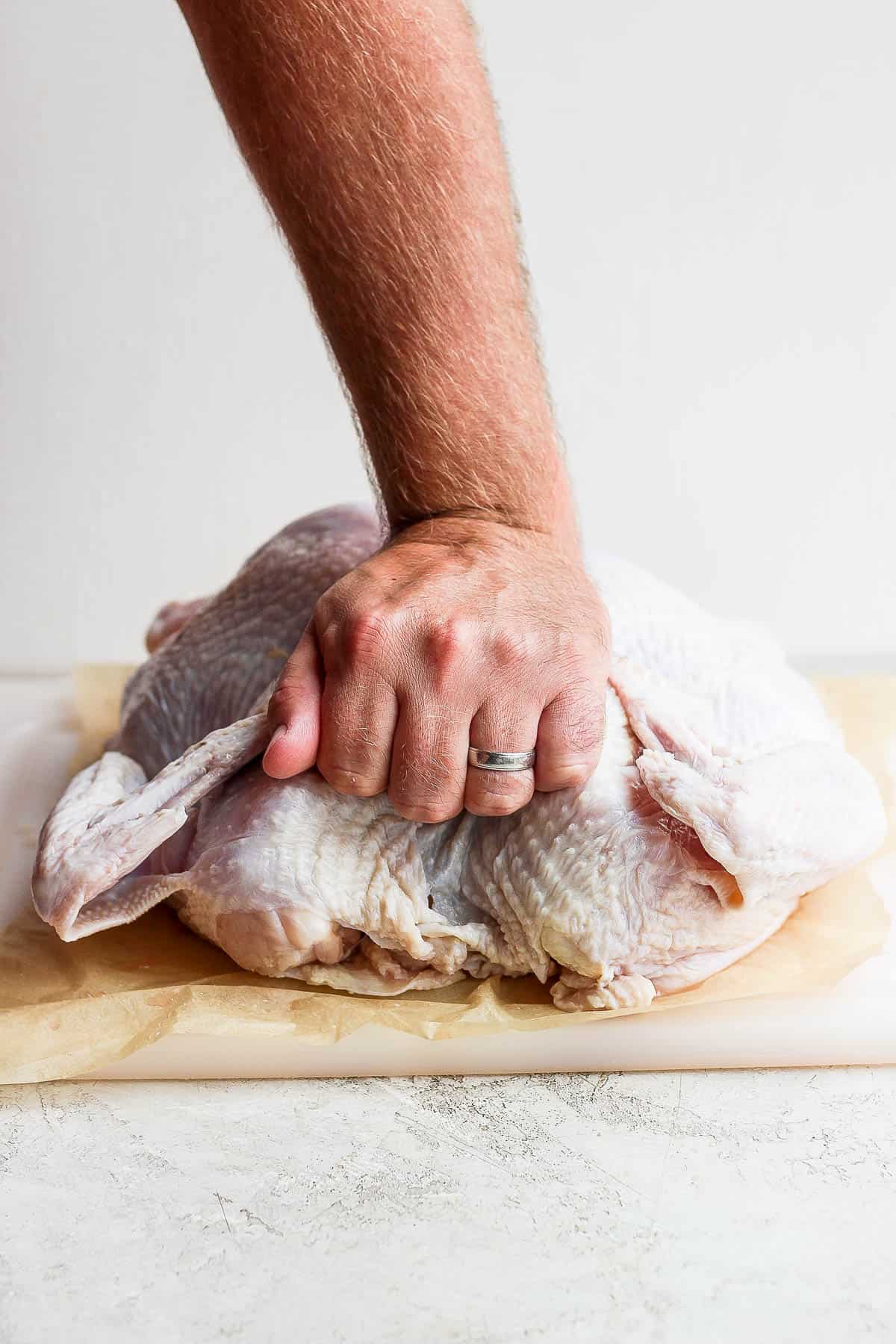 A hand pressing down on a turkey after the backbone was removed to flatten it.