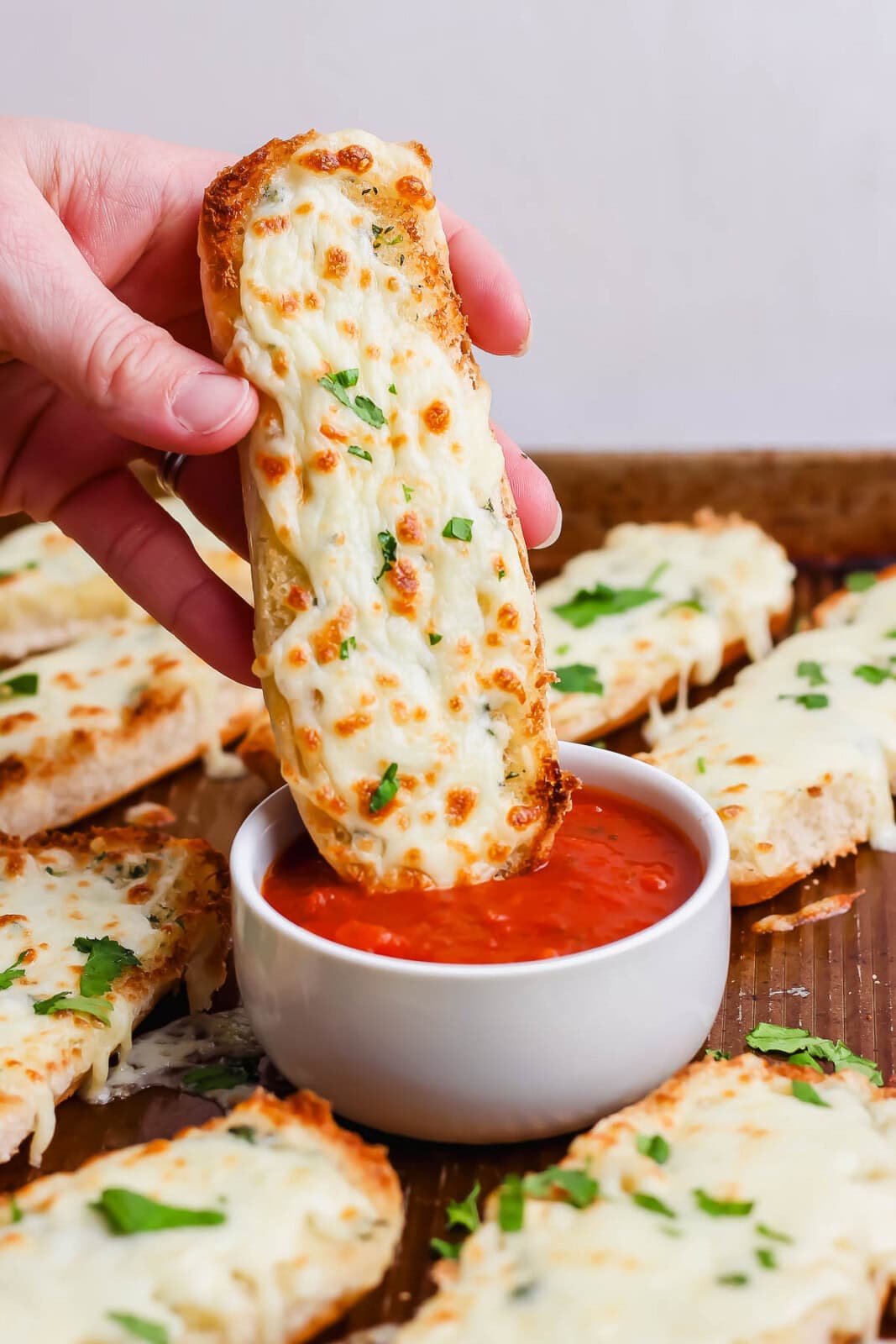 A hand holding an Italian dunker over a small bowl of marinara sauce.